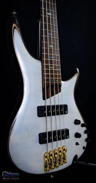 A white electric guitar with five strings and black knobs.