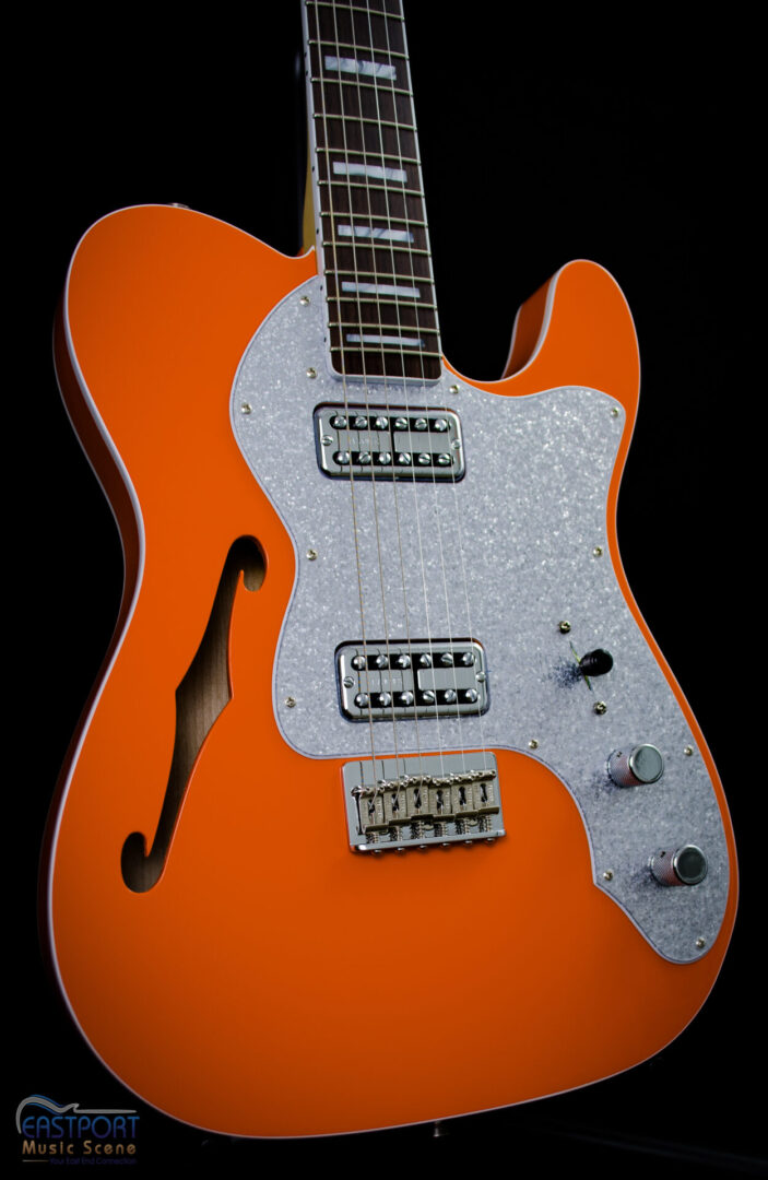 A close up of an orange guitar with silver accents