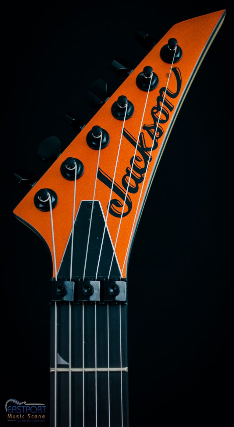 A close up of the neck and headstock of an orange guitar.
