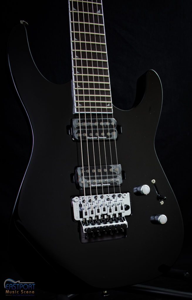 A black electric guitar with the strings and pick holes.