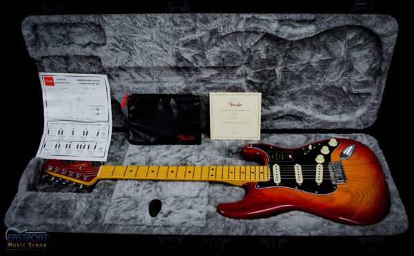A guitar laying on top of a bed next to some papers.